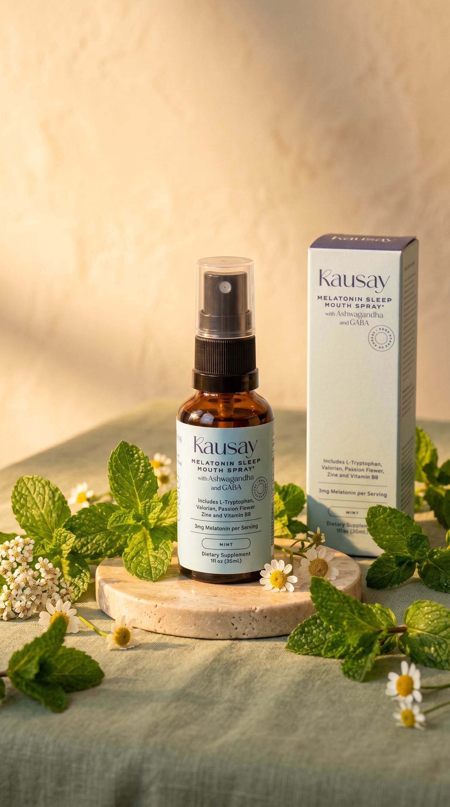 Kausay melatonin sleep mouth spray bottle and packaging styled with fresh mint leaves and chamomile flowers on a stone pedestal